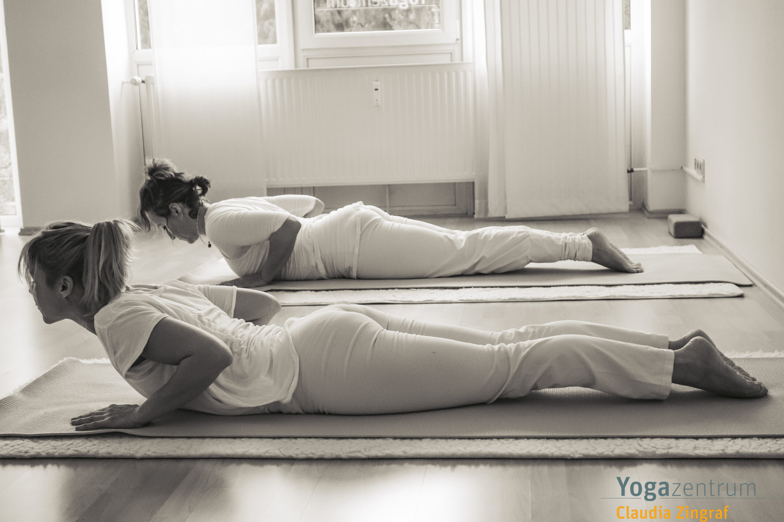 Zwei Frauen in der Kobra-Haltung (Bhujangasana) während einer Hatha-Yoga-Stunde bei Claudia Zingraf in Saarbrücken – achtsame Rückbeuge zur Stärkung des Rückens.