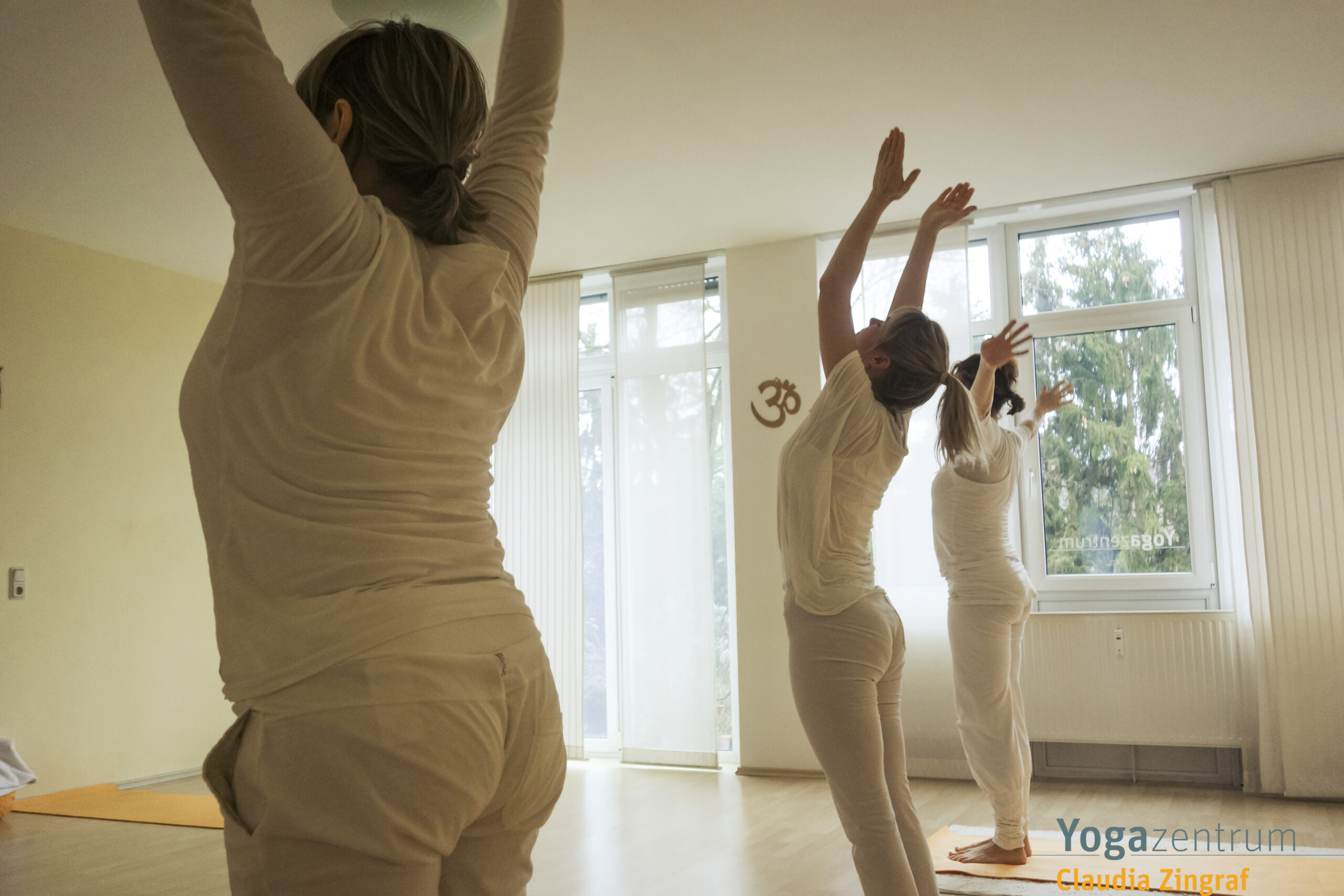 Drei Frauen in aufrechter Yoga-Haltung mit erhobenen Armen während einer Hatha-Yoga-Stunde bei Claudia Zingraf in Saarbrücken – achtsamer Beginn des Sonnengrußes.